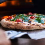 A margherita pizza with fresh basil leaves and tomatoes is being prepared in a gas oven for cooking pizza.