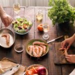 couple is cooking a shrimp dinner and a vegetable salad together. They're also both drinking white wine.