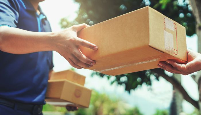 A close-up of a deliveryman delivering a parcel box to a customer. The deliveryman is holding two other boxes.