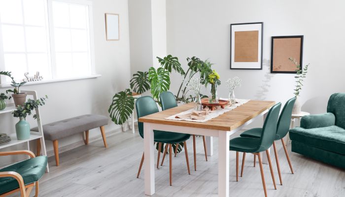 A brightly lit dining room with white walls. A wooden table with four dark green chairs is in the room.