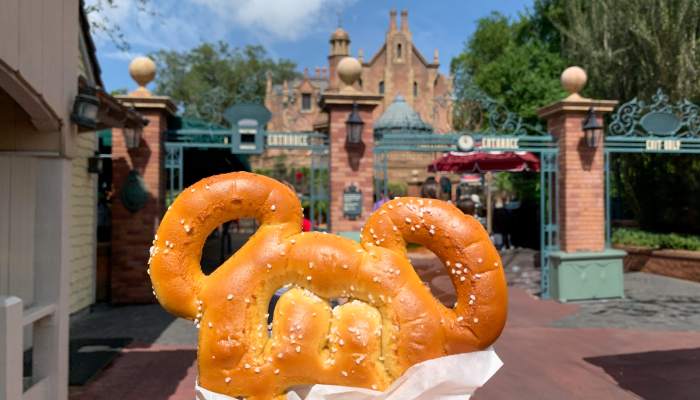 Home 18 A person holds a mouse-ear-shaped pretzel in front of a theme park attraction entrance.