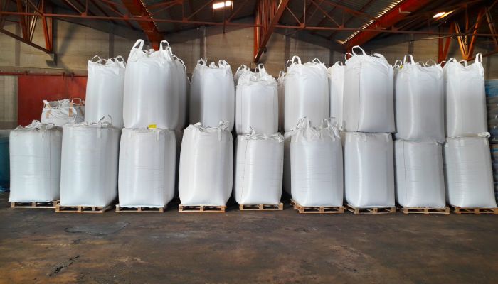 Large white farming fertilizer bags are in a warehouse. They are stacked on top of each other on pallets.