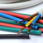A three-core cable with a gray cable jacket wrapped up on a white surface and sitting on a pile of heat shrink tubing.