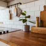 A dark brown wooden countertop in a residential kitchen. Two potted plants with green leaves are on the countertop.