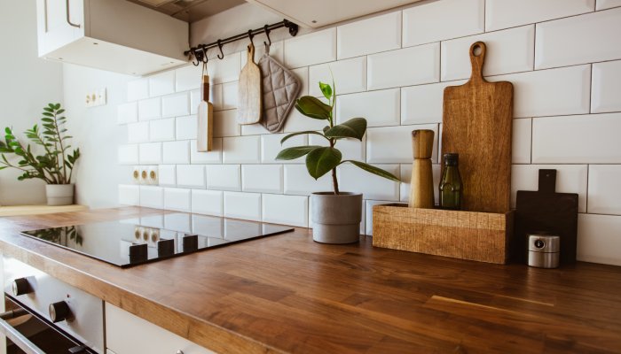 A dark brown wooden countertop in a residential kitchen. Two potted plants with green leaves are on the countertop.