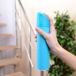 Someone holds a blue can of air freshener. Their finger hovers over the the button to spray the product.