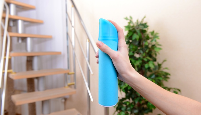 Someone holds a blue can of air freshener. Their finger hovers over the the button to spray the product.