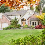 A two-story home sits at the end of a long driveway. It has brick and beige siding and a three-car, attached garage.