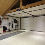 A garage features a white-tiled floor, an organization system with shoes and tools, a wooden ceiling, and a white garage door.