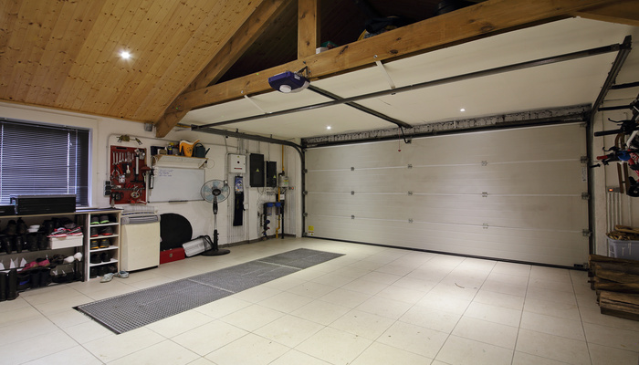 A garage features a white-tiled floor, an organization system with shoes and tools, a wooden ceiling, and a white garage door.