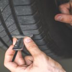 A close-up of a professional mechanic's hand checking the depth of a car tire tread and doing car maintenance.