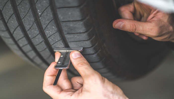 A close-up of a professional mechanic's hand checking the depth of a car tire tread and doing car maintenance.