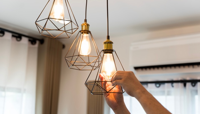 A person using their bare hands to replace the bulb inside a pendant light hanging from the ceiling in a home.