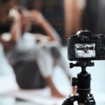 A close-up view shows a black, high-end digital camera sitting on a black tripod, taking a photo of a person doing a sit-up.